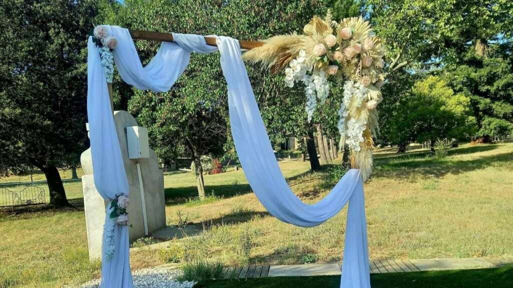 Location arche de mariage - une belle arche bohême dans un champs avec des voilages blancs et bouquets de pampa