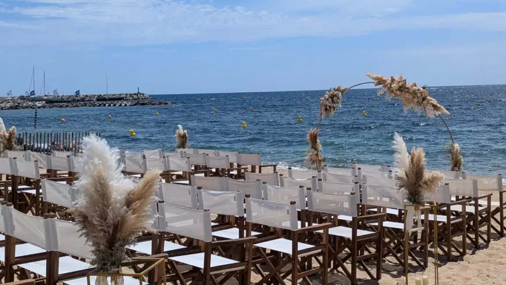 Décoration d'une cérémonie laïque sur la plage de saint maxime pour un mariage, allée de chaises en bois avec arche ronde et allée de cérémonie décoré en bouquet de pampa