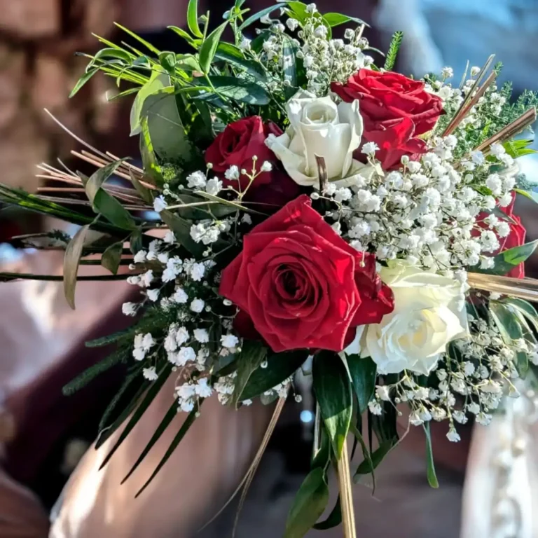 Bouquet de mariée romantique avec des roses rouges et blanches, entouré de gypsophile et de feuillage vert, parfait pour un mariage sur le thème de l'amour et de la passion dans le Var. Composition florale élégante, mettant en valeur la beauté des roses fraîches, idéale pour une cérémonie de mariage raffinée.