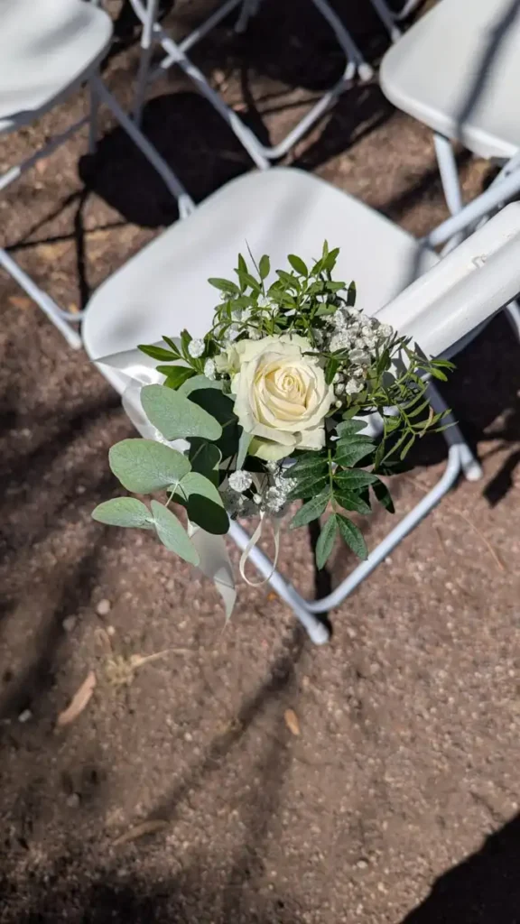 Gerbes de fleurs fraîches avec roses blanches pour décoration de chaises de mariage, disponibles chez Iliade Location dans le Var. Élément de décoration élégant et romantique pour cérémonie en plein air.