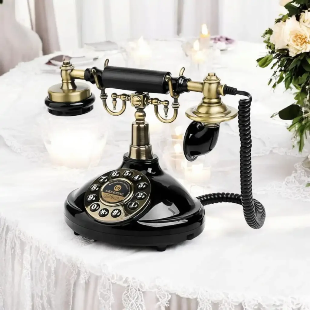 Ancien téléphone à cadran noir et doré utilisé comme livre d'or audio pour un mariage, posé sur une table élégamment décorée avec des fleurs et des bougies, créant une ambiance romantique