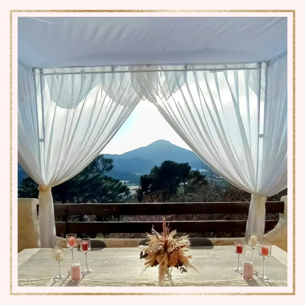 Location houppa métal blanc mariage Var : arche carrée en métal blanc ornée de voilages légers, installée en terrasse avec vue panoramique sur les collines du Var, idéale pour une cérémonie de mariage en plein air.