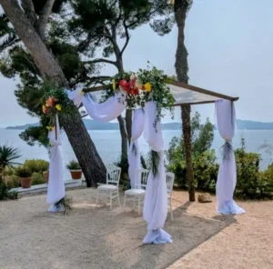 Houppa en bois avec voilage blanc et composition florale colorée, installation élégante pour cérémonie de mariage en bord de mer.