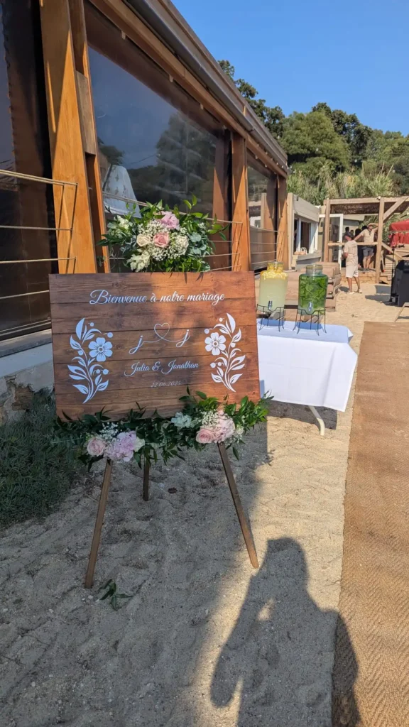 Panneau de bienvenue en bois personnalisé pour mariage à la plage au Coco Beach La Fossette, décoré de fleurs fraîches et feuillages.