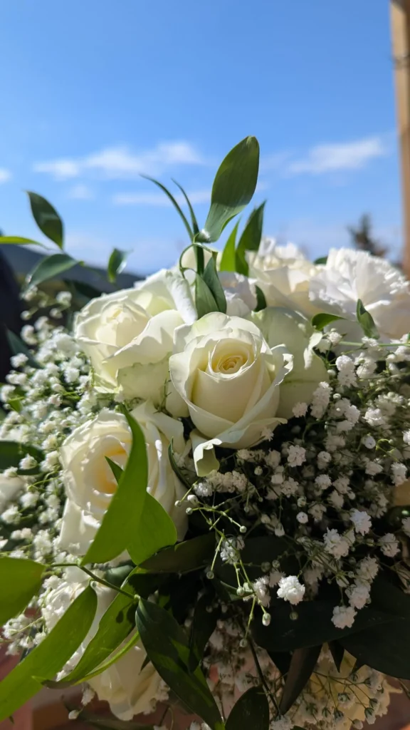 Bouquet de mariée déstructuré composé de roses blanches, gypsophile et feuillage ruscus avec ruban ivoire.