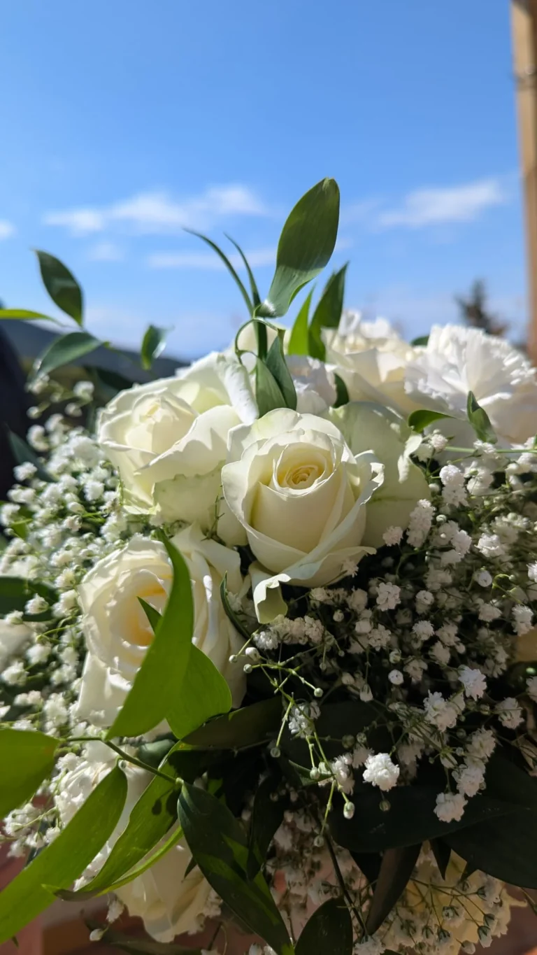 Bouquet de mariée déstructuré composé de roses blanches, gypsophile et feuillage ruscus avec ruban ivoire.