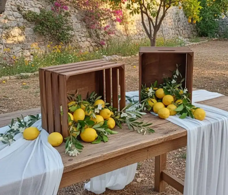 Mise en scène de mariage Dolce Vita sur table en bois avec caisses rustiques remplies de citrons et de branches d’olivier, ambiance méditerranéenne naturelle.