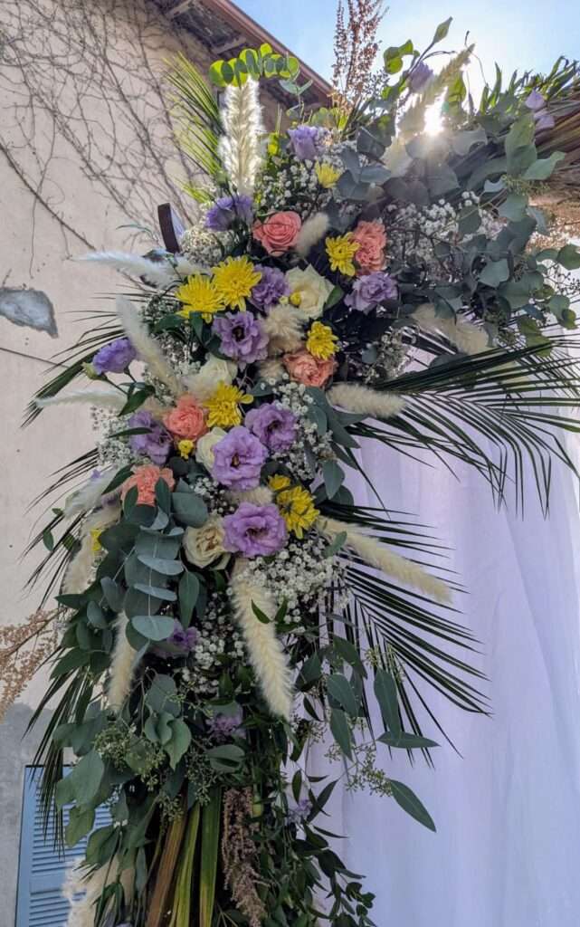 Composition florale pastel pour arche de cérémonie, avec lisianthus mauve, roses saumon, pampa et eucalyptus.