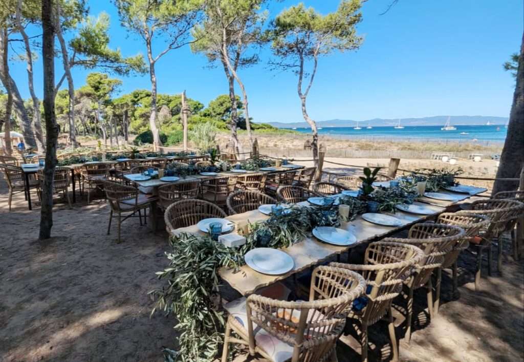 Table de mariage en plein air face à la mer, décorée de guirlandes d’olivier et de vaisselle en céramique dans une ambiance bois naturel et bleu marine. Le noé plage Hyères 83400