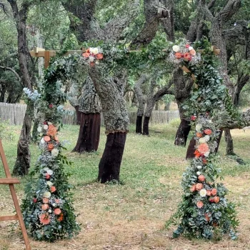 Arche de cérémonie de mariage en fleurs fraîches dans une forêt, ornée de feuillage vert et de roses dans les tons corail et blanc, au Domaine du Vieux Sauveur près du Lavandou.