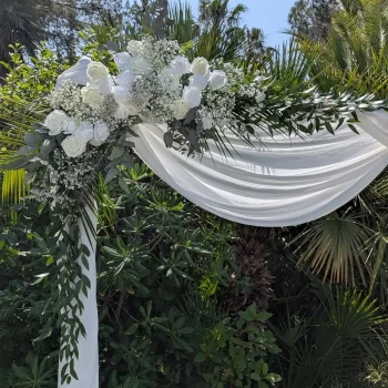 Arche de cérémonie laïque décorée de fleurs blanches et feuillages, drapée de tissu blanc élégant pour mariage en extérieur.