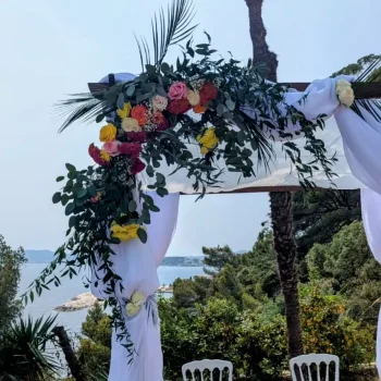 Arche houppa en bois décorée de fleurs colorées et feuillages, pour une cérémonie de mariage en plein air face à la mer.