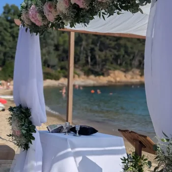 Décoration florale raffinée sur houppa en bois pour cérémonie de mariage dans le Var, fleurs fraîches blanches et roses sur fond de mer Méditerranée.
