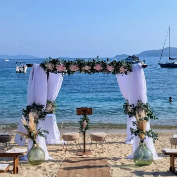 Houppa en bois pour cérémonie de mariage sur la plage au Coco Beach La Fossette, décorée à la main avec fleurs fraîches blanches et roses pastel.
