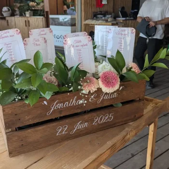 Plan de table mariage personnalisé dans une caisse en bois avec feuillage frais et fleurs pastel, décoration champêtre et élégante pour réception dans le Var.